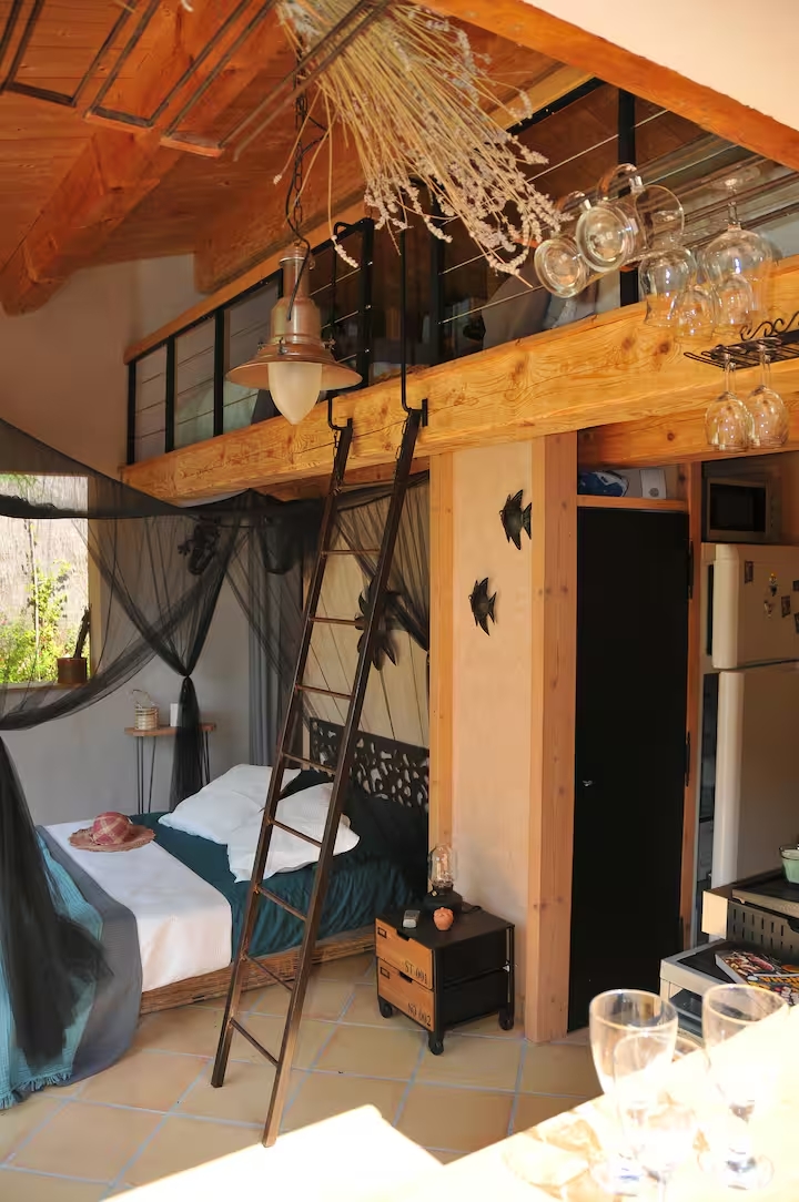 Chambre atypique avec un lit double sous baldaquin noir, une échelle de meunier menant à une mezzanine et une décoration chaleureuse en bois.
