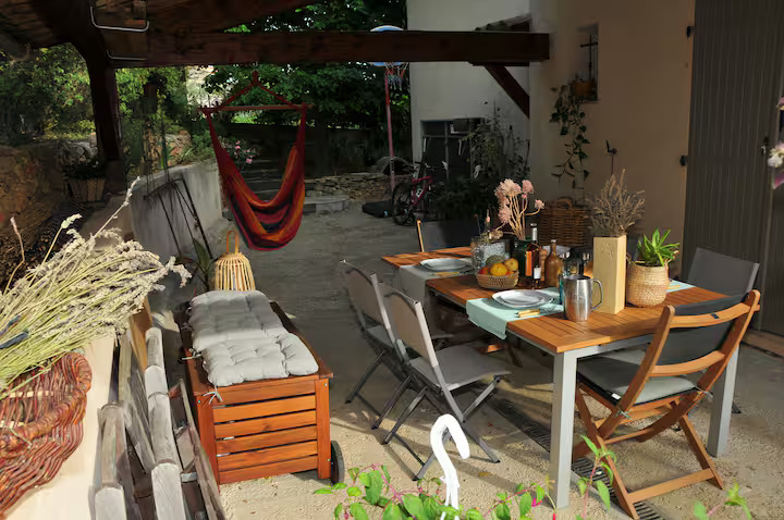 Terrasse couverte avec une grande table à manger en bois dressée, un hamac coloré suspendu et un coin salon cosy pour les repas en plein air.