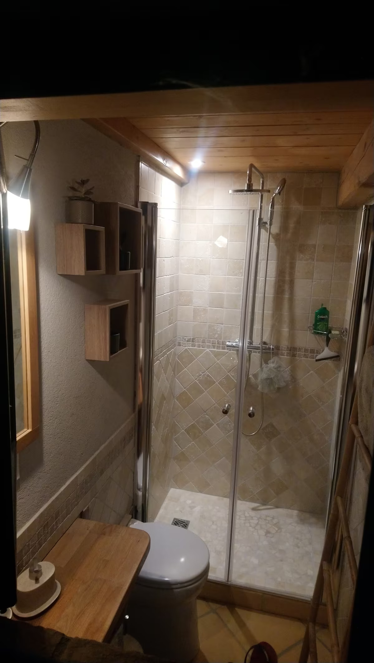 Salle d'eau moderne avec douche à l'italienne carrelée en tons pierre, vasque sur plan de travail en bois et étagères murales épurées.